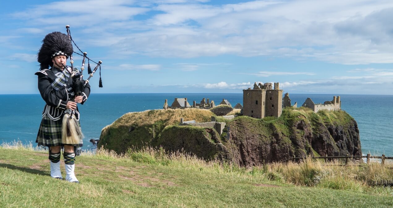 Vista del Castillo de Dunnottar junto a un escocés tocando la gaita